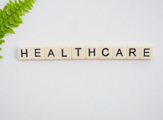 Tessere con la scritta HEALTHCARE su sfondo chiaro con foglia verde nell’angolo, immagine simbolica dedicata al settore sanitario.