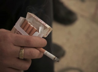 Mano che tiene una sigaretta accesa e un pacchetto di sigarette